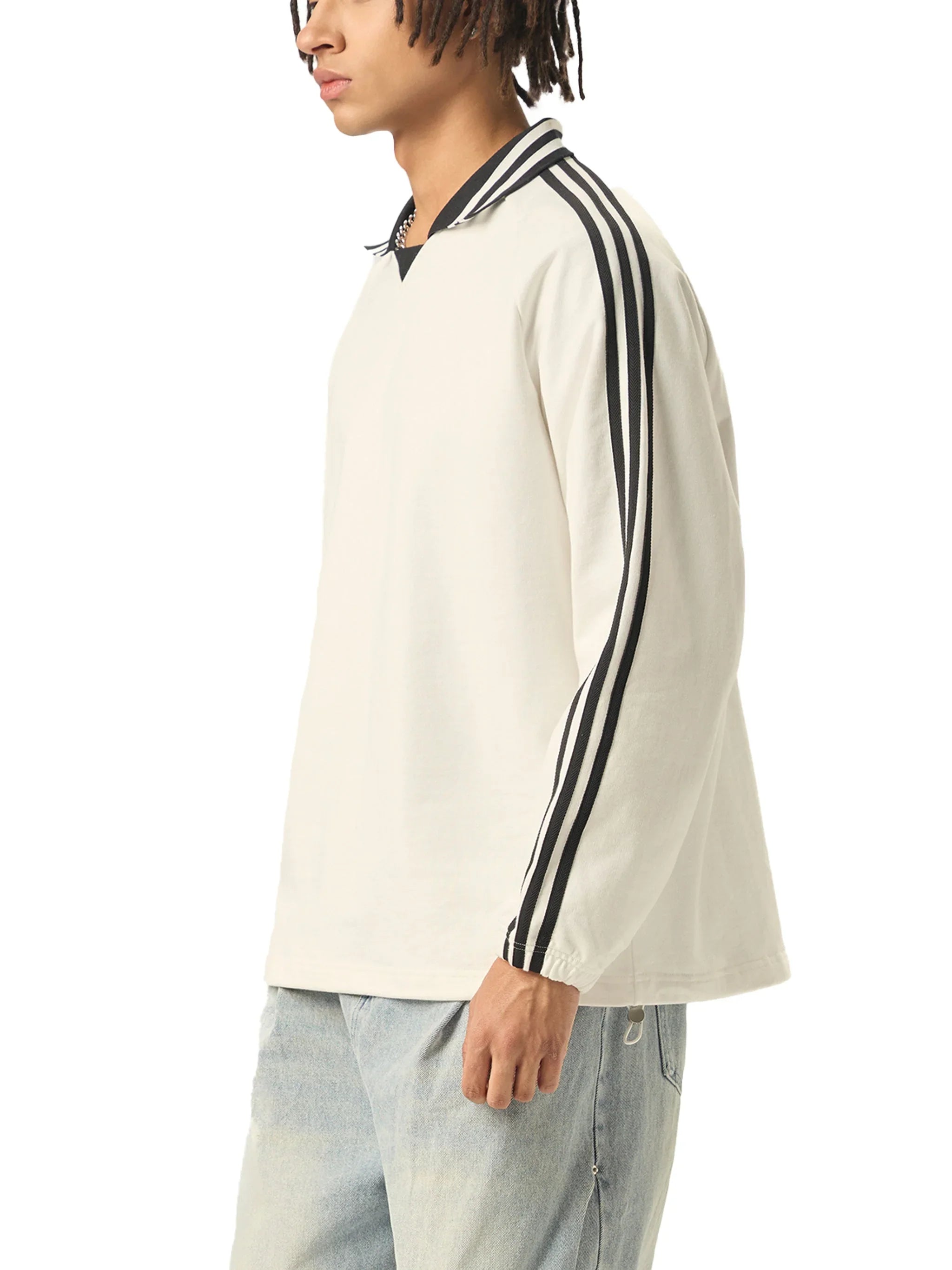 Man wearing a white long sleeve streetwear top with black striped sleeves and light washed jeans
