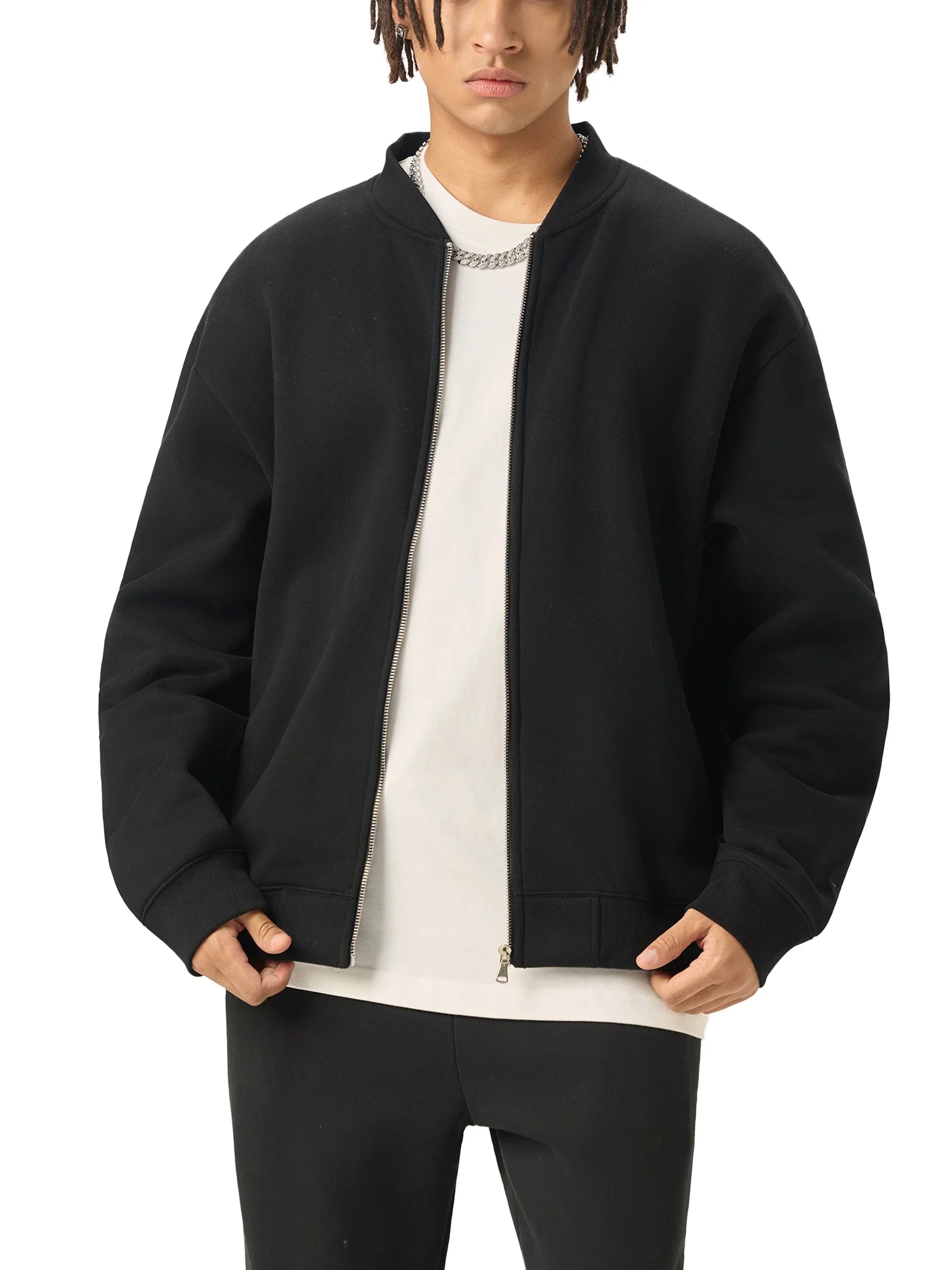 Man wearing a black zip-up bomber jacket over a white t-shirt and black pants, streetwear style