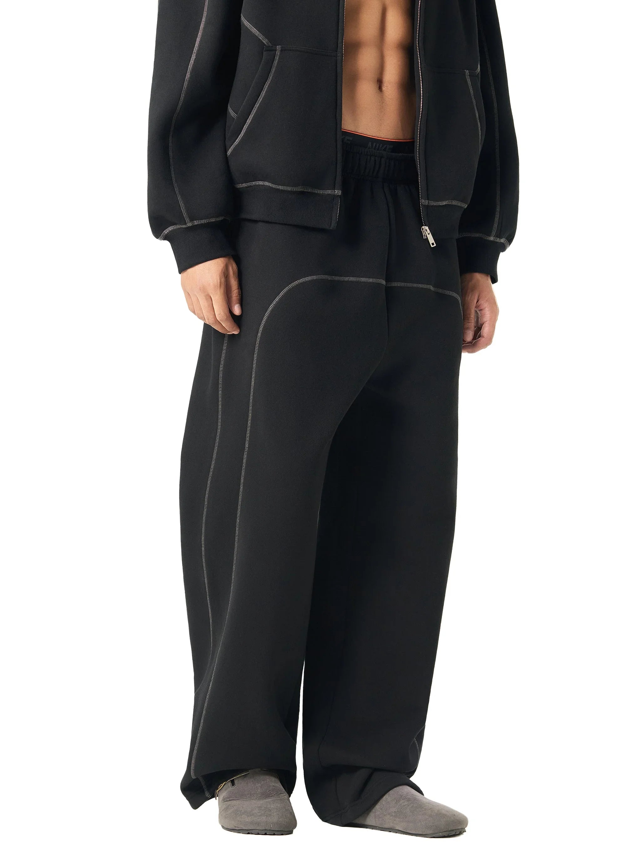 Man wearing black heavyweight wide-leg sweatpants with contrast stitching and grey slippers